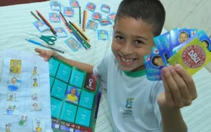 O menino João Gabriel, de 8 anos, com o álbum da Panini e o que desenhou: "Gosto dos dois" - Foto: Fábio Lima/O Popular